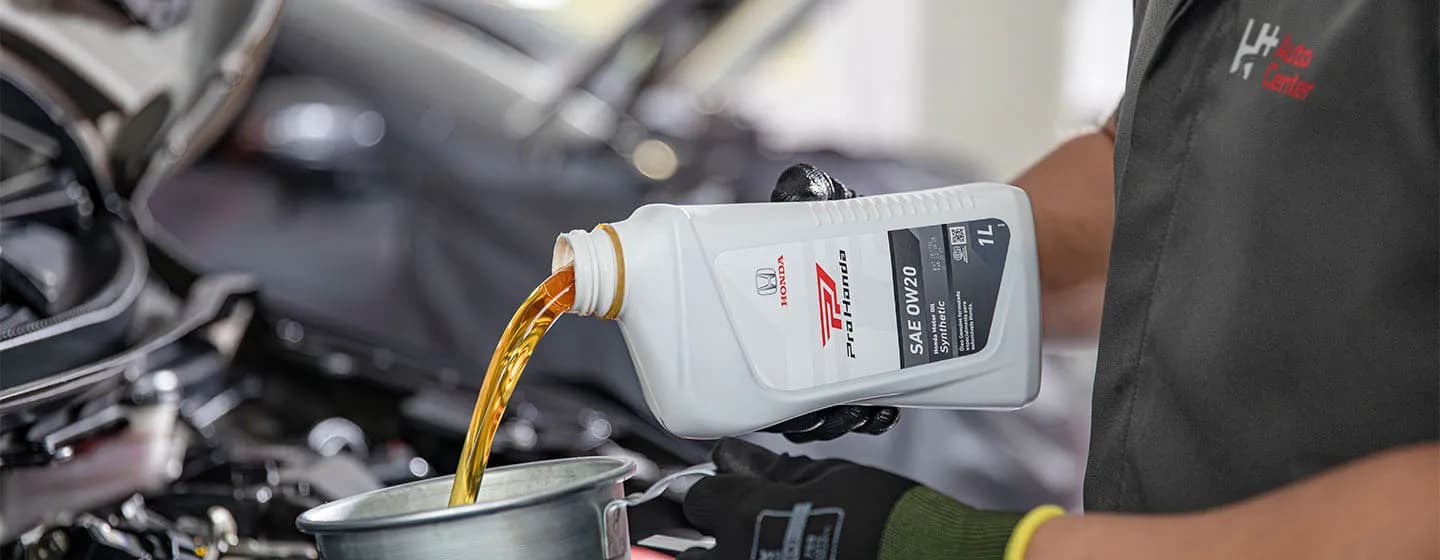 Mecanico segurando uma lata de óleo em frente a um carro com o capô aberto e preenchendo o motor com óleo