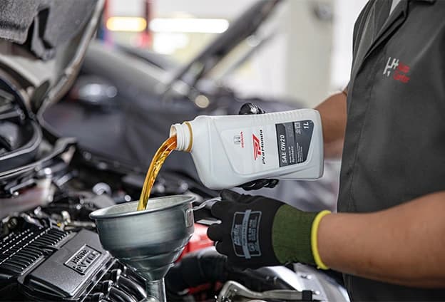 mecanico derramando óleo em um funil para colocar no motor de um carro