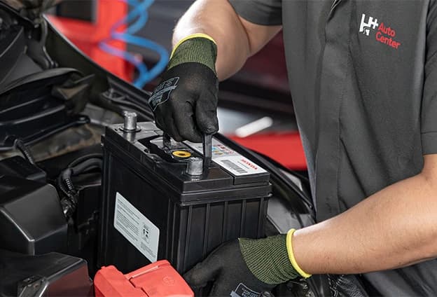 mecanico segurando uma bateria automotiva em frente ao capô aberto de um carro